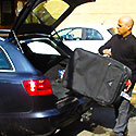 a airport taxis driver helping with loading a customers black suitcase into a black audi airport taxis
