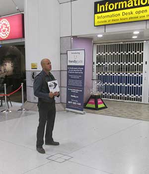 distance photo of our airport taxis cab driver inside manchester airport smartly dressed holding a sign to meet and greet a customer