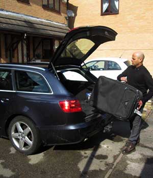 corner view of a airport taxis driver loading a customers large black suitcase into the back of a black audi a6 estate airport taxis cab